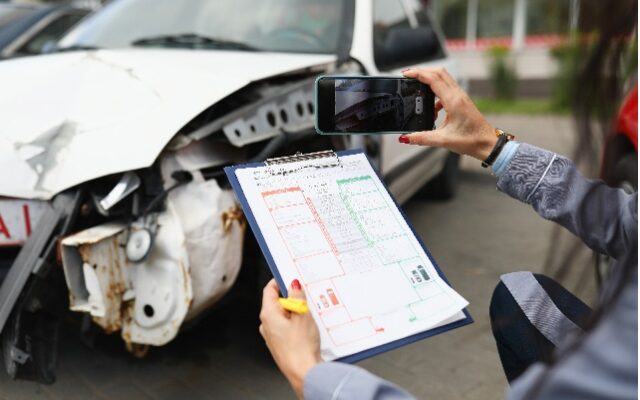Insurance agent takes pictures of crashed car on his smartphone and fills out the insurance